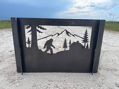 Steel panel cut with a skunk ape walking past pines, a cabin and mountains