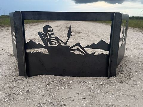 Steel panel cut with a skeleton in a lounge chair holding a bottle, mountains behind