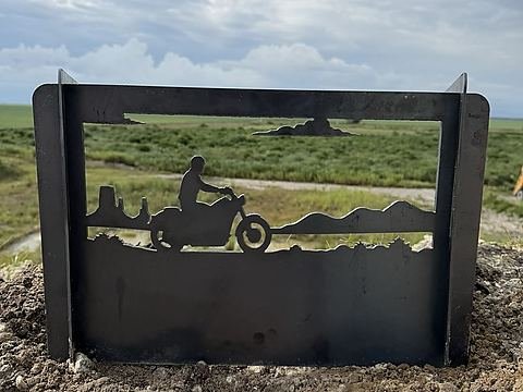 Steel fire pit panel with a motorcycle rider cruising past buttes and desert hills