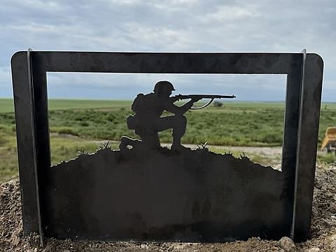 Steel fire pit panel with a kneeling soldier taking aim on a grassy ridge