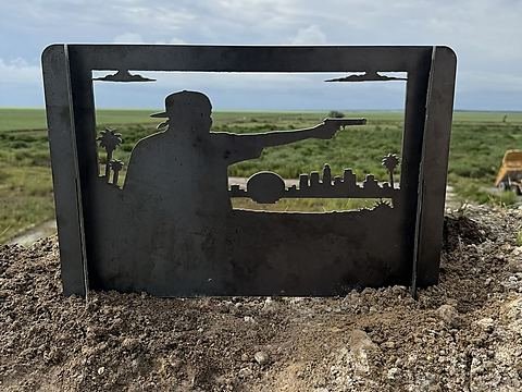Steel fire pit panel with a figure in a ball cap over a palm-lined city skyline at sunset